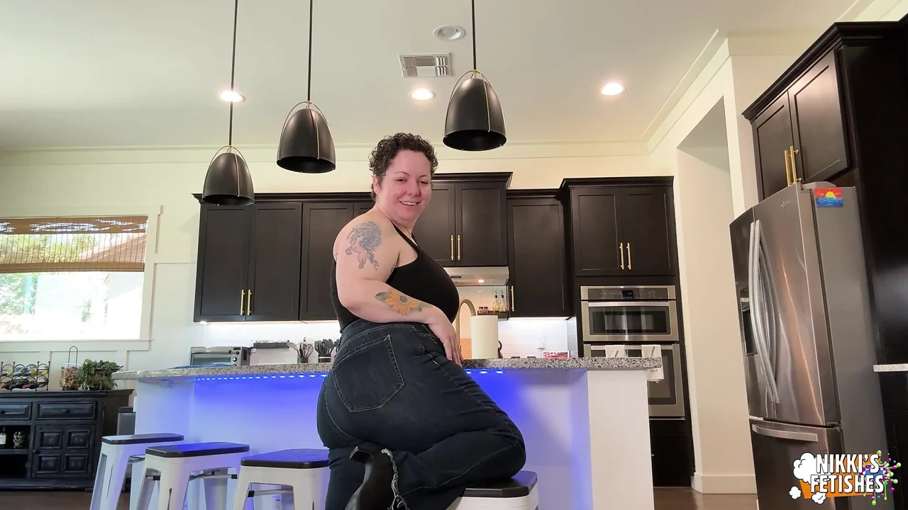 穿着牛仔裤的NIKKISFETISHES纹身女人在柜台上弯下腰，在凳子上摆姿势